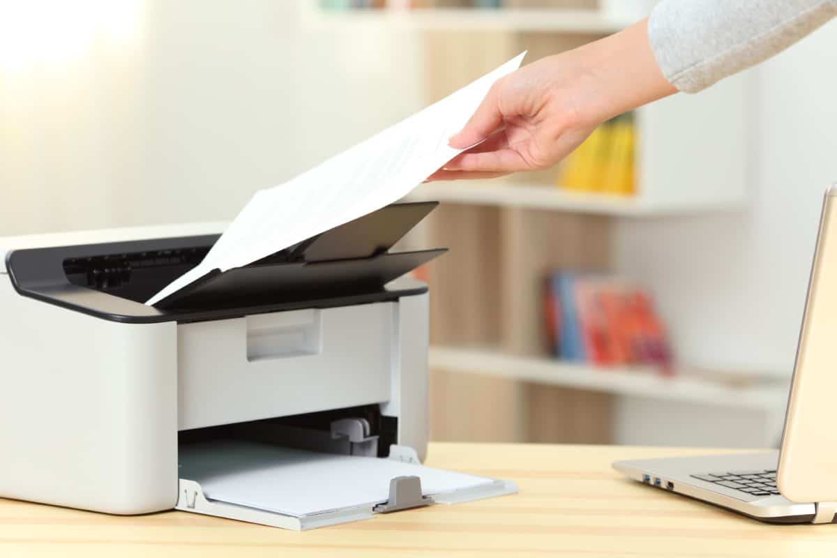 Close up of a woman hand catching a document from a printer on a desk at home