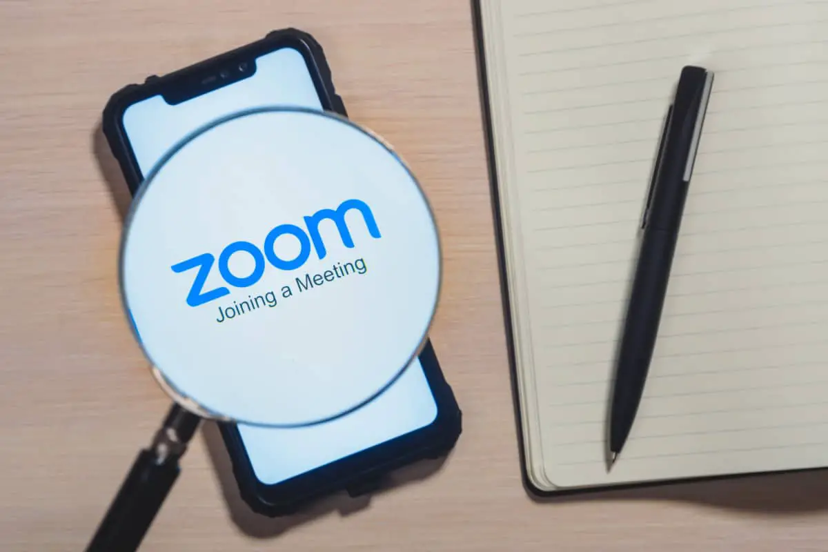Zoom app logo on the screen smartphone closeup. Zoom Video Communications is a company that provides remote conferencing services. Daily planner with a pen.
