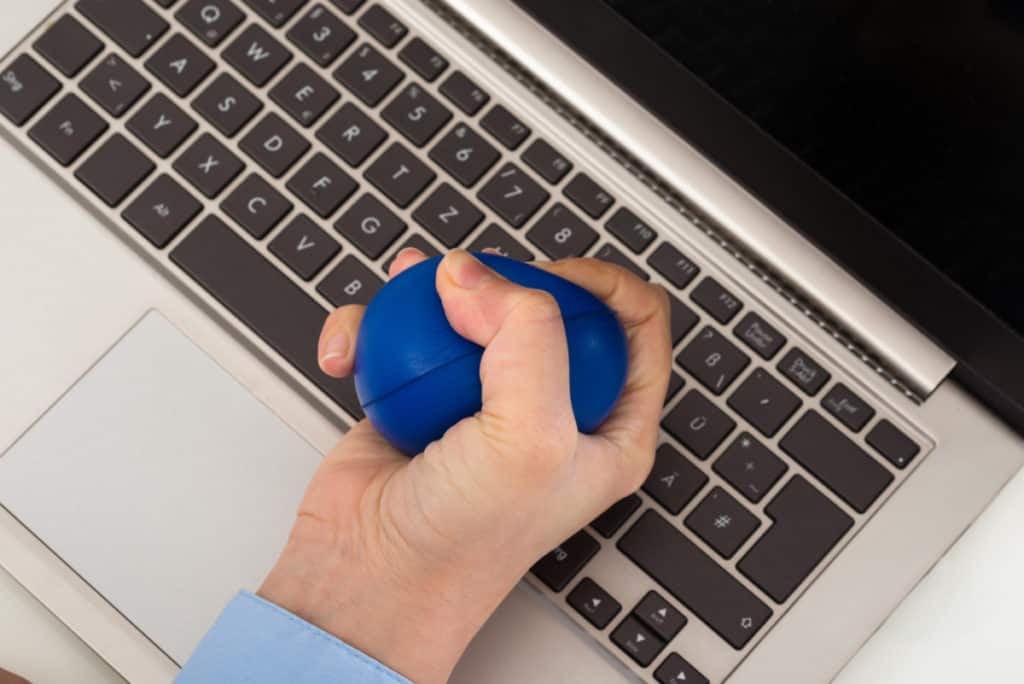 Close-up Of Businesswoman Hand Over Laptop Squeezing Stressball