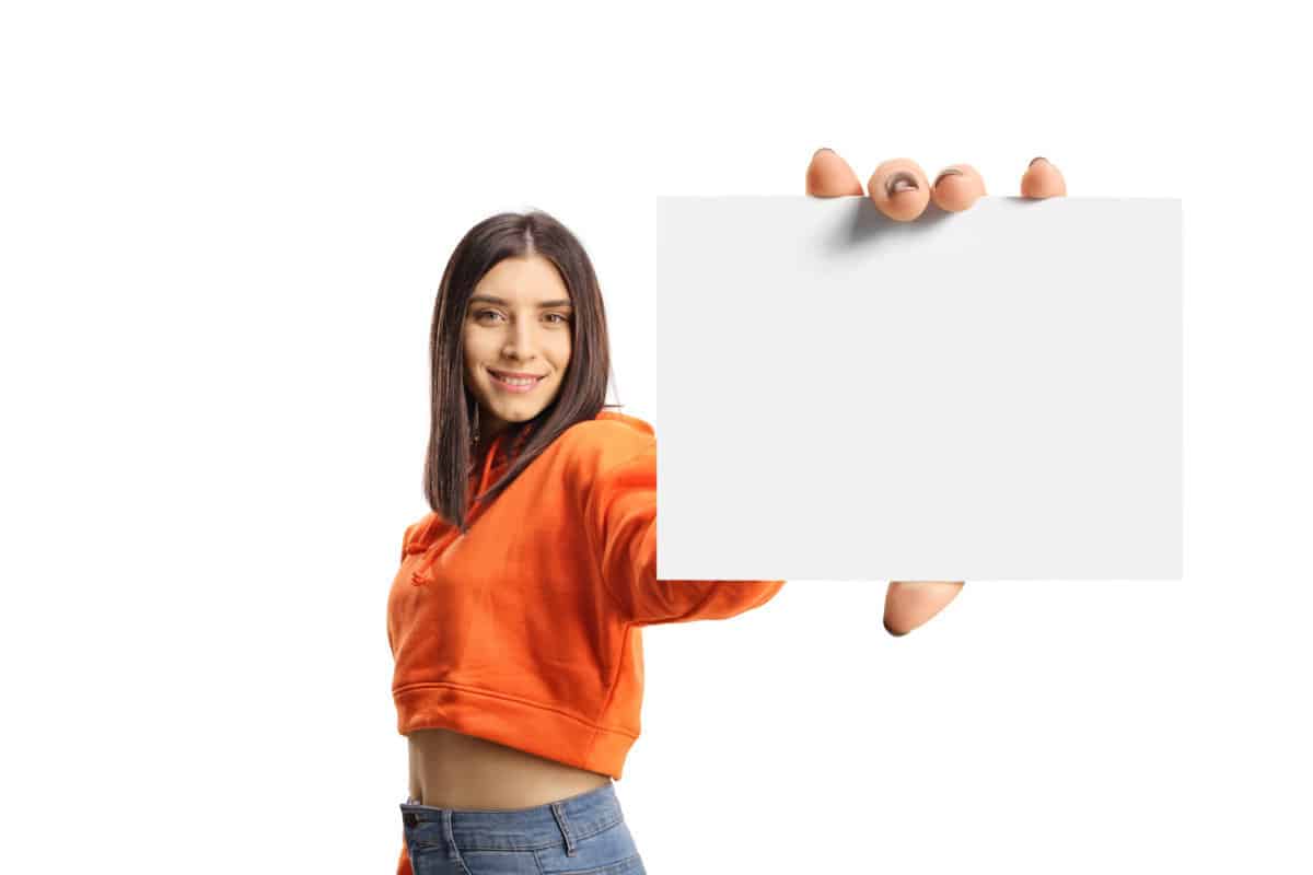 Young female in an orange sweatshirt showing a blank id card isolated on white background