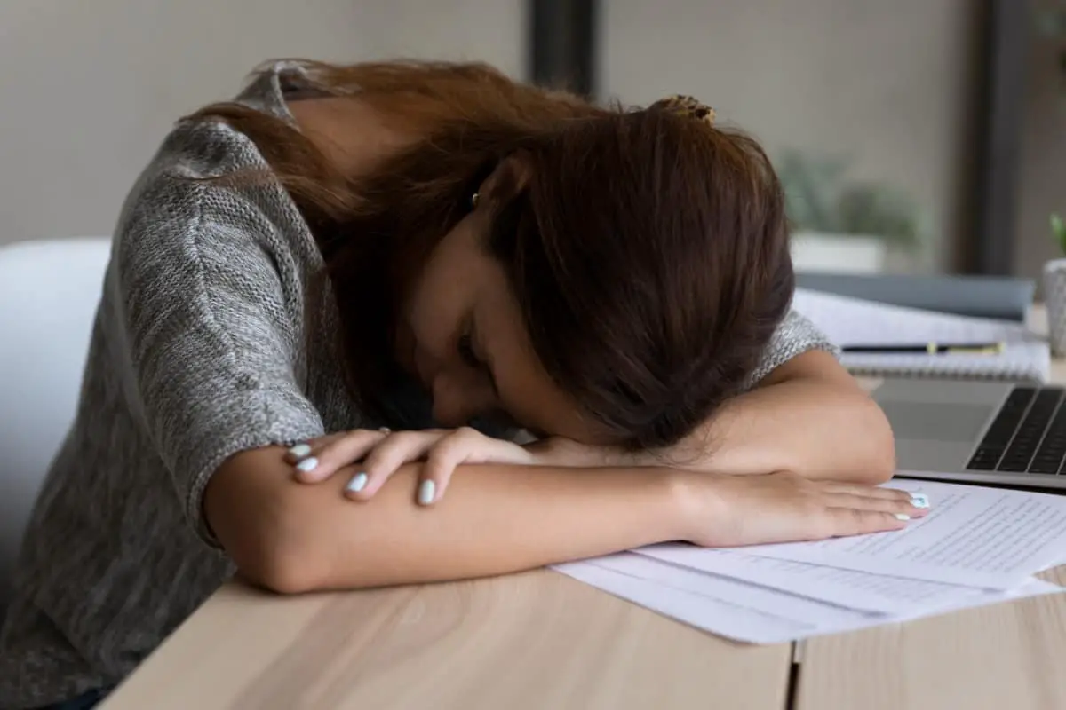Exhausted millennial female employee worker fall asleep lying on table, overwhelmed with work, tired young Caucasian woman sleep take nap at workplace, feel fatigue exhaustion, overwork concept
